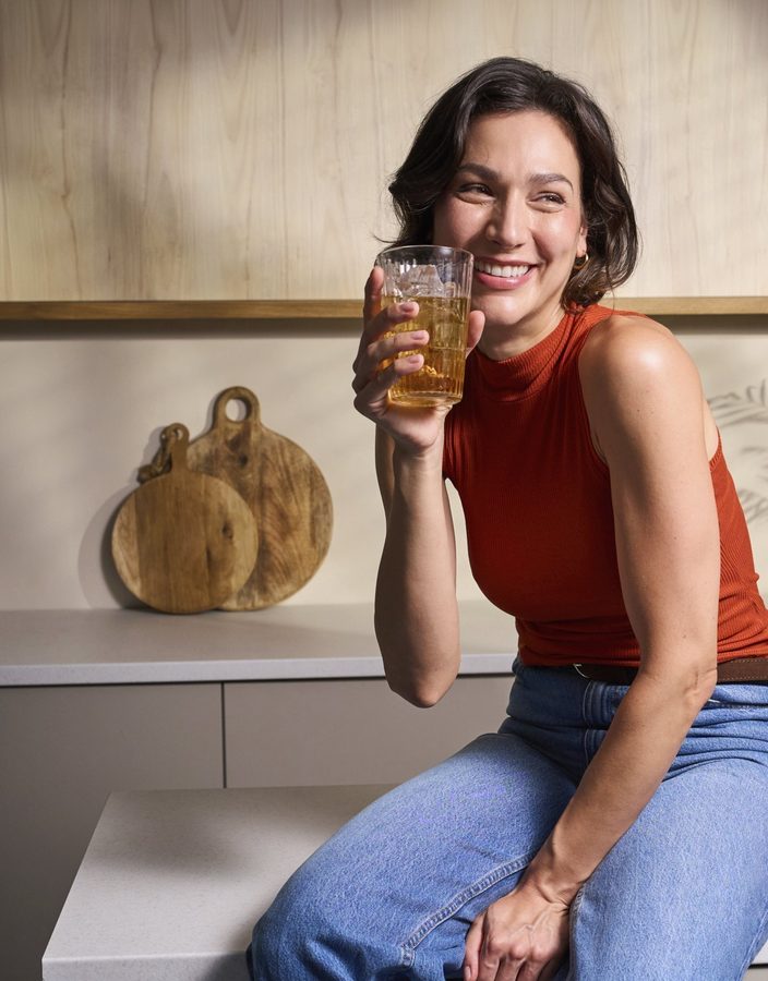 Donna che ride la mattina nella sua cucina con un bicchiere in mano, piena di energia